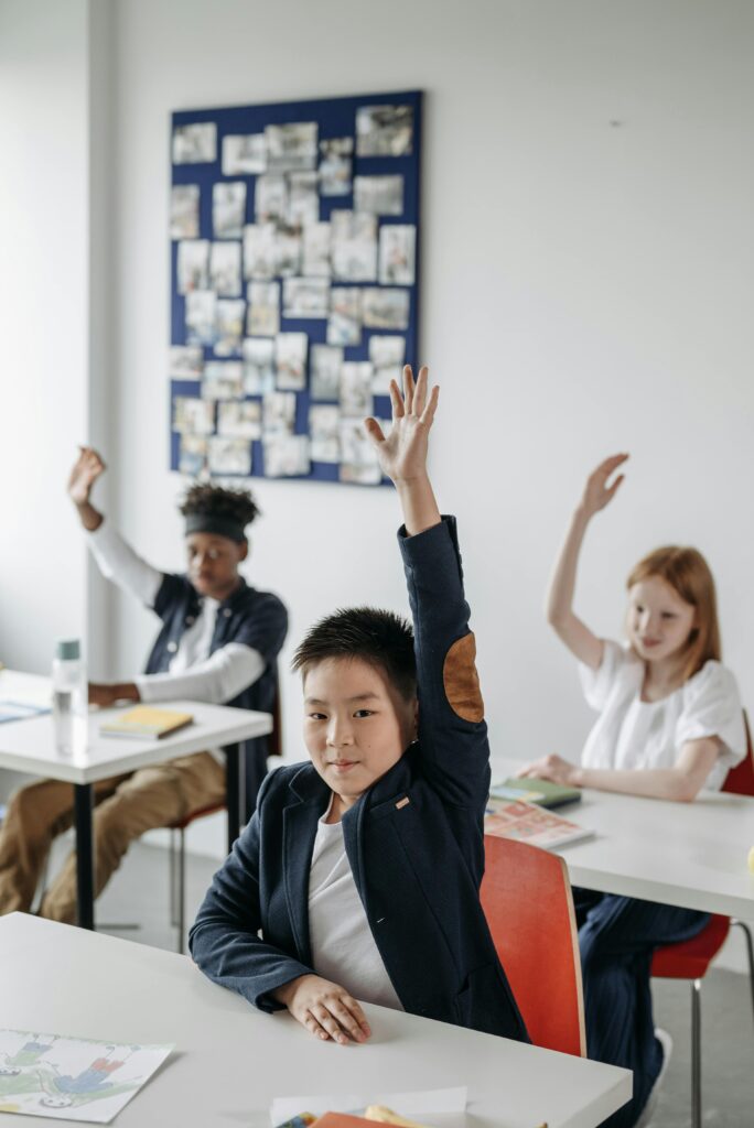pexels-photo-8423045-8423045 Children in a modern classroom raise hands during an engaging lesson.